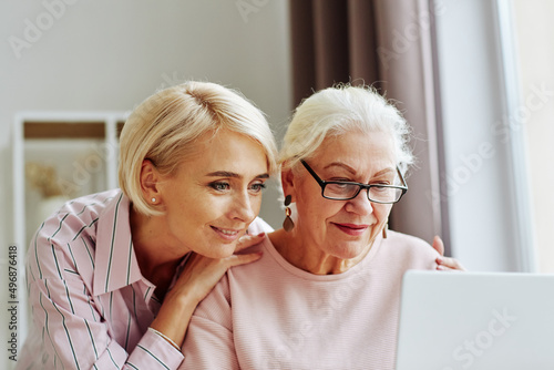 Close up portrait of young woman with senior mother using computer together at home and shopping online