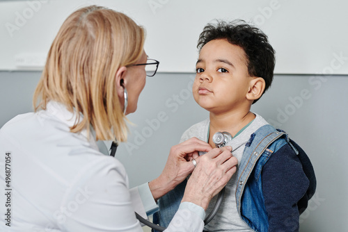 Cute sick little boy in casualwear sitting by wall of medical office while having treatment during visit pediatrician in modern hospital