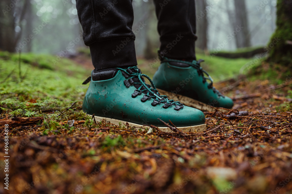 Feet in green boots in the untouched forest through the moss, close photo. Tourism concept. Hiking in the mountains.