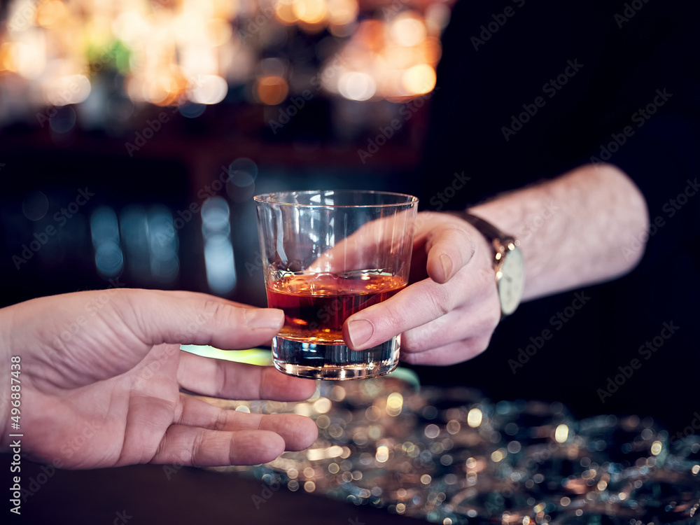 Hands of a pub customer and bartender serving a glass of neat whiskey. Close up view.