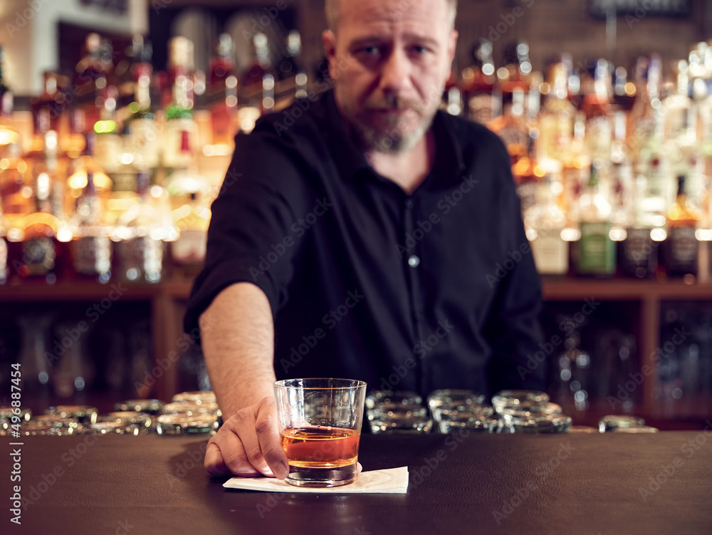 Male bartender serves a glass of neat whiskey at the pub