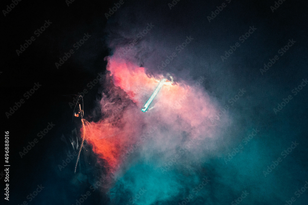 A man in a gas mask with an umbrella and colored smoke, photo at night