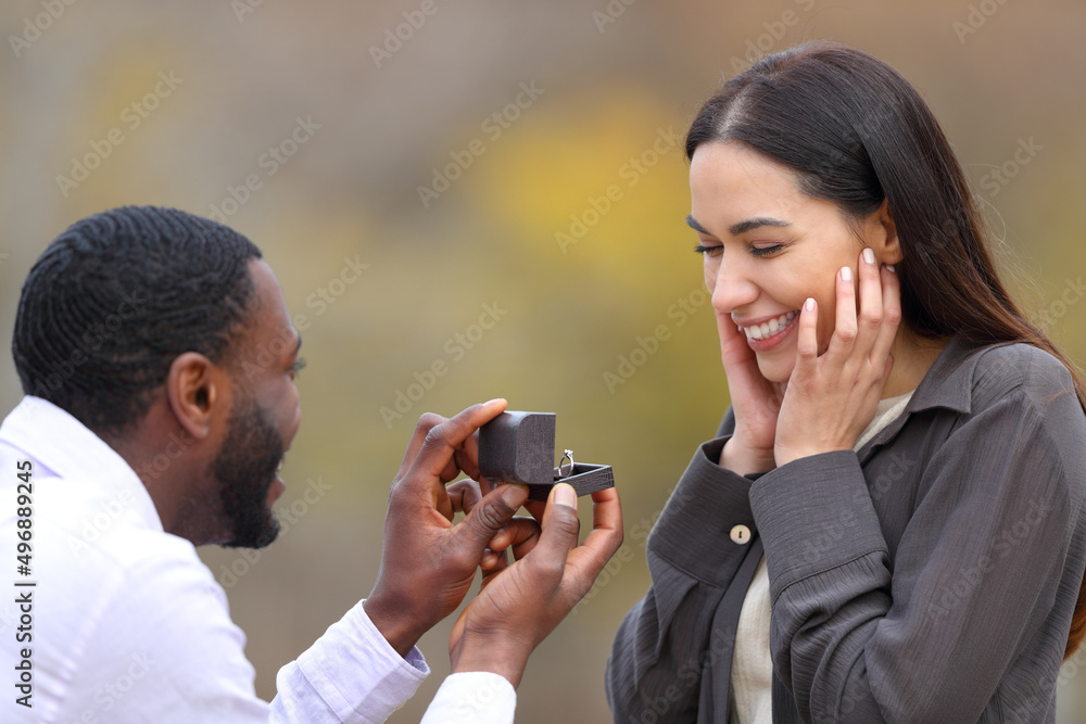 Interracial couple proposing marriage in a park - obrazy, fototapety, plakaty 