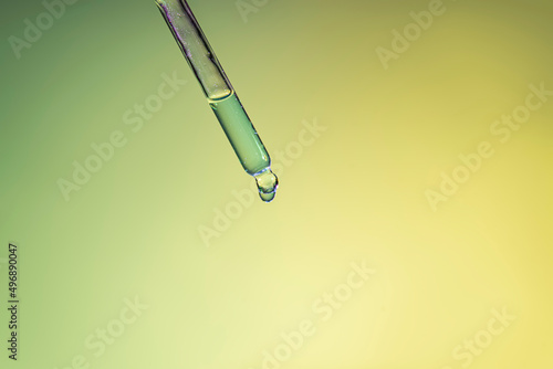 Liquid serum and dropper on purple and yellow background.