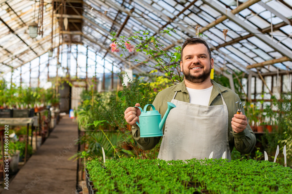 A smiley young man with watering can in a greenhouse. A smiley young man with watering can in a greenhouse.