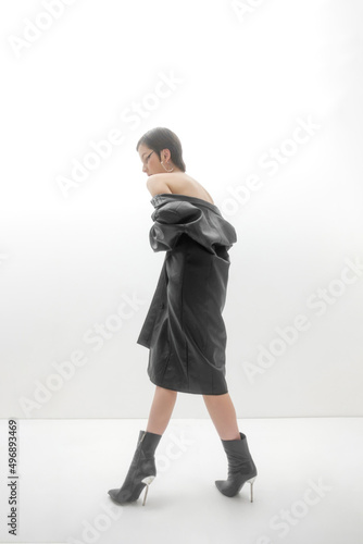 Fashion photo shoot in studio, on white background. Young beautiful woman emotionally and dramatically poses in black vintage cloak on a naked body. Short brown hair, large black eye arrows.