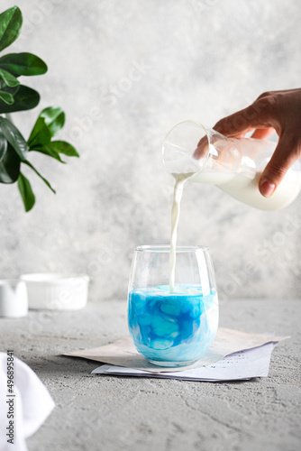 glass of blue cocktail. Blue cocktail with milk and ice on the gray background. Bottle with milk in the hand 