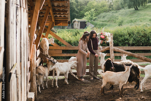 Romantic, young and happy caucasian couple in stylish clothes traveling together on the sheep farm in beautiful nature. Love, relationships, romance, animal care, happiness concept.