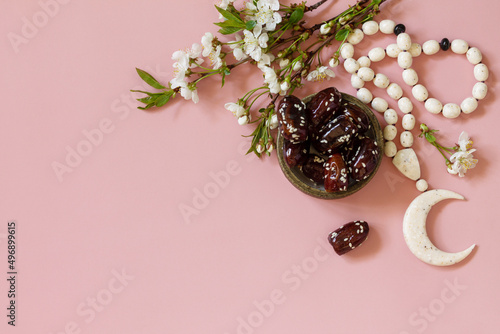 Ramadan food and drinks concept. Ramadan Islamic rosary beads, white flowers and dates fruit on a light pink background. Iftar dinner. Top view flat lay. Copy space. photo