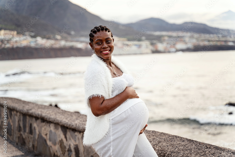 Beautiful pregnant woman in white clothes posing on the ocean coast, smiling and looking at the camera. Future motherhood concept. Mom to be Beautiful pregnant woman in white clothes posing on the ocean coast, smiling and looking at the camera. Future motherhood concept. Mom to be