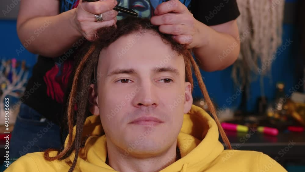 Unrecognizable person makes hairstyle for young man in salon. Professional hairstylist makes brown dreadlocks for client. Unrecognizable person makes hairstyle for young man in salon. Professional hairstylist makes brown dreadlocks for client.