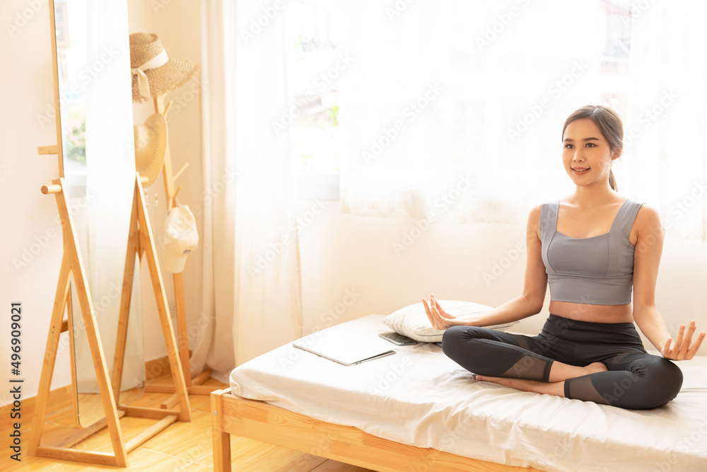 Young Asian woman is exercising yoga at home. Fitness, workout, healthy living and diet concept. Female watching videos online on laptop computer in bedroom. Young Asian woman is exercising yoga at home. Fitness, workout, healthy living and diet concept. Female watching videos online on laptop computer in bedroom.