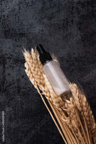 Concept natural herbal organic cosmetic. Facial serum in dropper glass bottle and dried ears of wheat on bark background. Vertical photo, place for text, poster.
