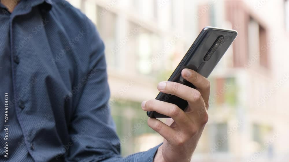 A man looks at a smartphone in an urban area - closeup - office buildings in the blurry background A man looks at a smartphone in an urban area - closeup - office buildings in the blurry background