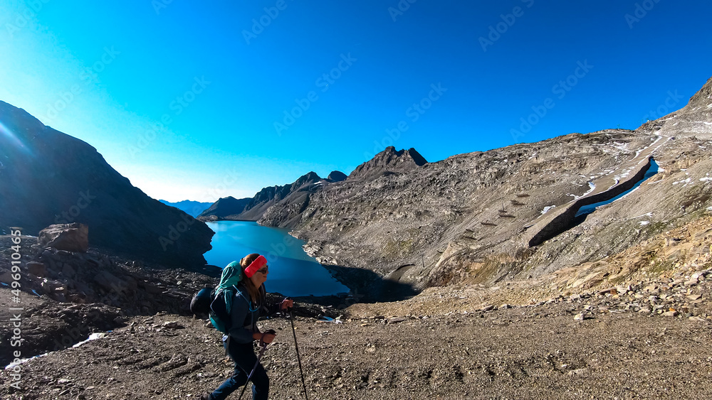 Woman with big backpack hiking with a scenic view on the mountains of Hohe Tauern Alps in Carinthia, Austria, Europe. A lake and water reservoir in the moelltaler glacier. Hohe Tauern National Park