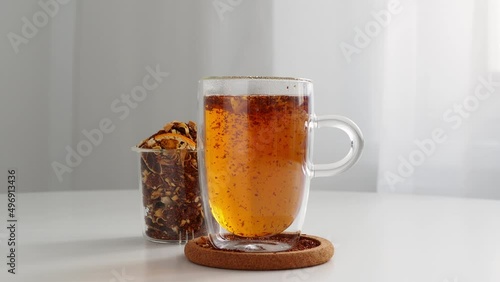 Rooibos tea brew in a transparent glass thermos that keeps the heat. Visualization of the process of brewing tea. The movement of tea leaves in a circle. Mug on the table. Welding in a jar. Tea ceremo photo