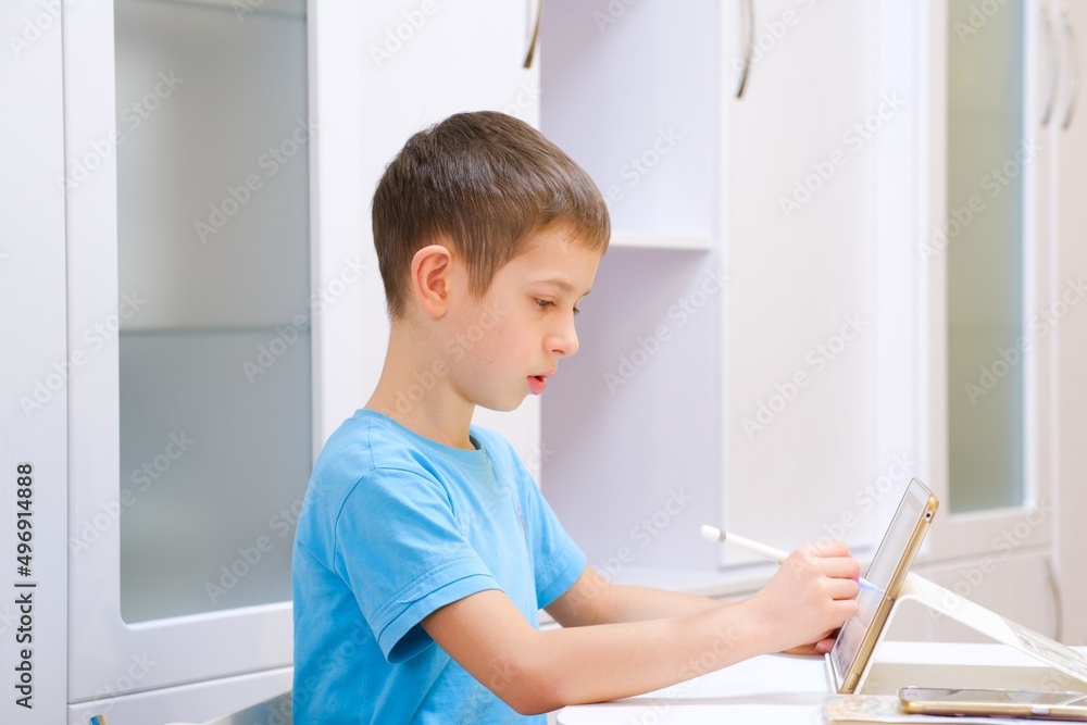 Boy of primary school age studies, draws on a tablet with wireless stylus. Crafting. Creativity. Kids using technology. Preparation for school. Classes for children of preschool and primary school age Boy of primary school age studies, draws on a tablet with wireless stylus. Crafting. Creativity. Kids using technology. Preparation for school. Classes for children of preschool and primary school age