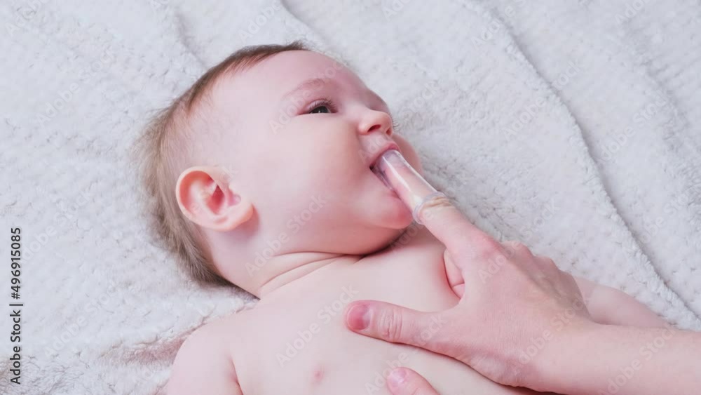 Mother hands brushing teeth with a finger brush of a happy infant baby. Mom doing oral hygiene to a smiling toddler kid, eight months old Mother hands brushing teeth with a finger brush of a happy infant baby. Mom doing oral hygiene to a smiling toddler kid, eight months old