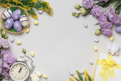 Fototapeta Naklejka Na Ścianę i Meble -  Easter concept on a gray background. Violet flowers and blooming yellow twigs gift eggs in a basket alarm clock.