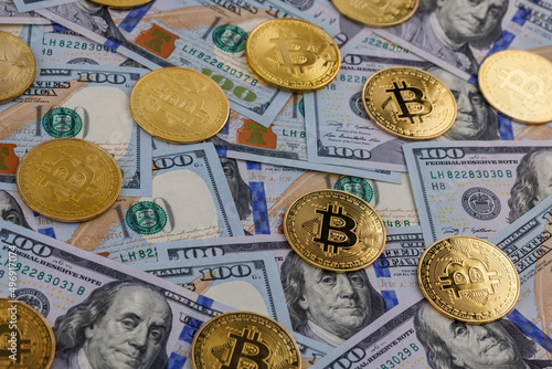 yellow bitcoin coins scattered over US dollar paper banknotes, closeup with selective focus photo