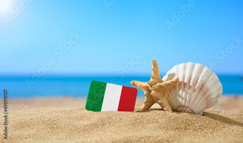 Fototapeta Naklejka Na Ścianę i Meble -  Tropical beach with seashells and Italy flag. The concept of a paradise vacation on the beaches of Italy and Sardinia.