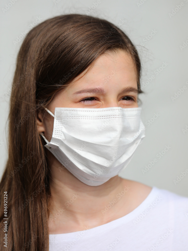 girl with long brown hair and smiling eyes with white mask to protect herself from coronavirus