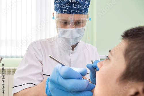 Male dentist curing patient's teeth. Stomatologist working with professional equipment in clinic office.