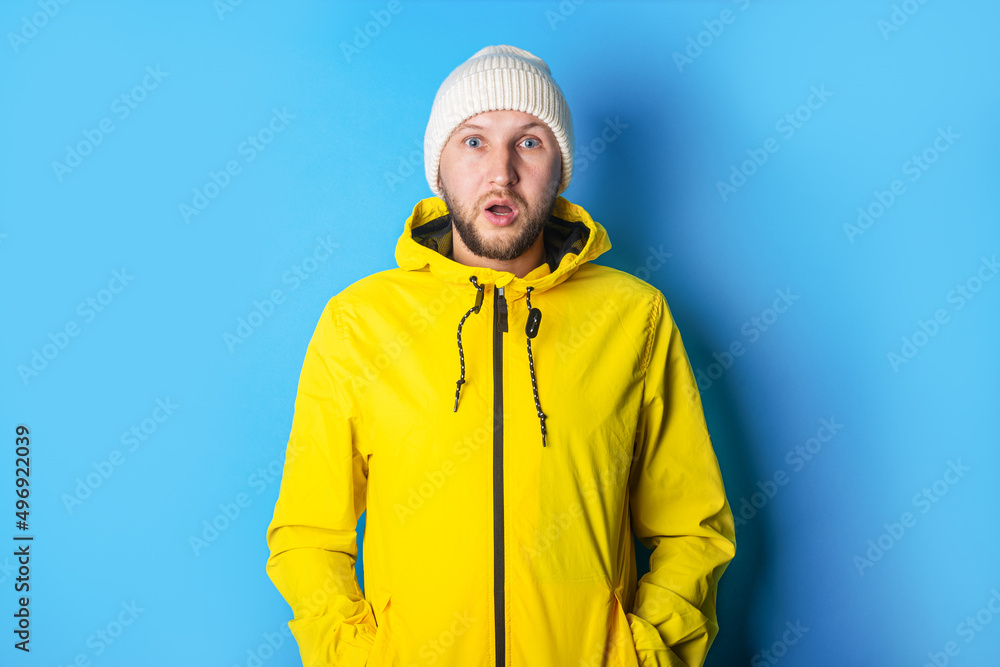 Surprised young man in a yellow jacket with a white hat on a blue background Surprised young man in a yellow jacket with a white hat on a blue background