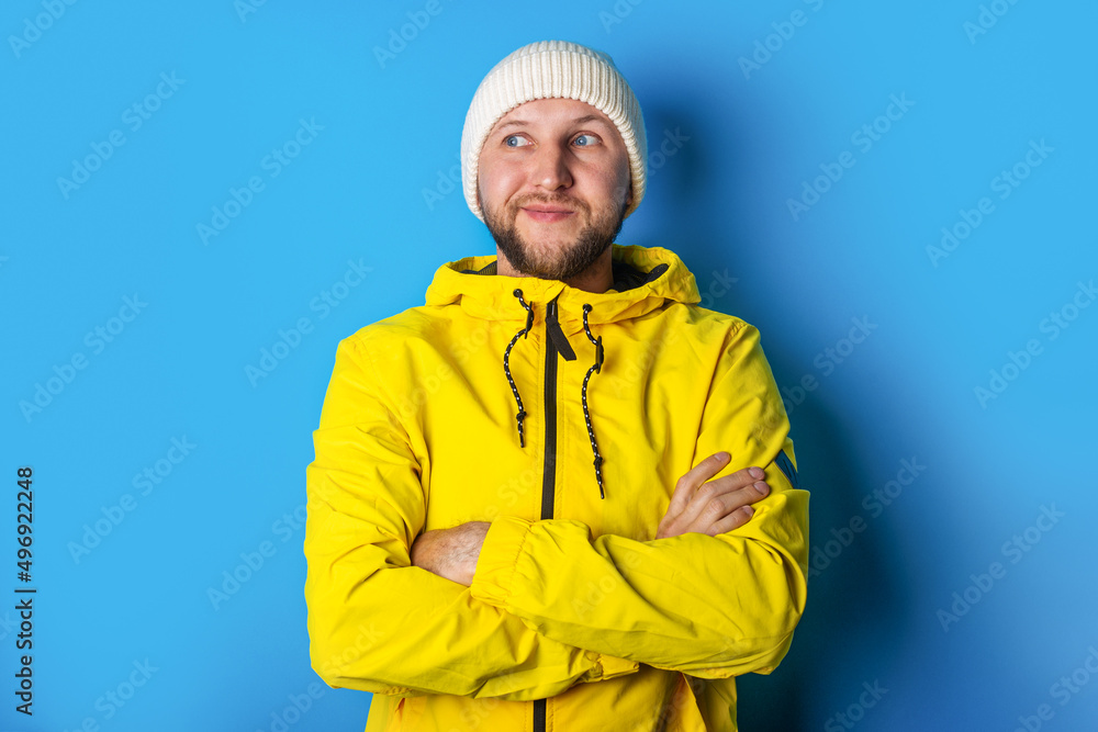 pensive young man in yellow jacket holds his arms crossed looking to the side on a blue background pensive young man in yellow jacket holds his arms crossed looking to the side on a blue background