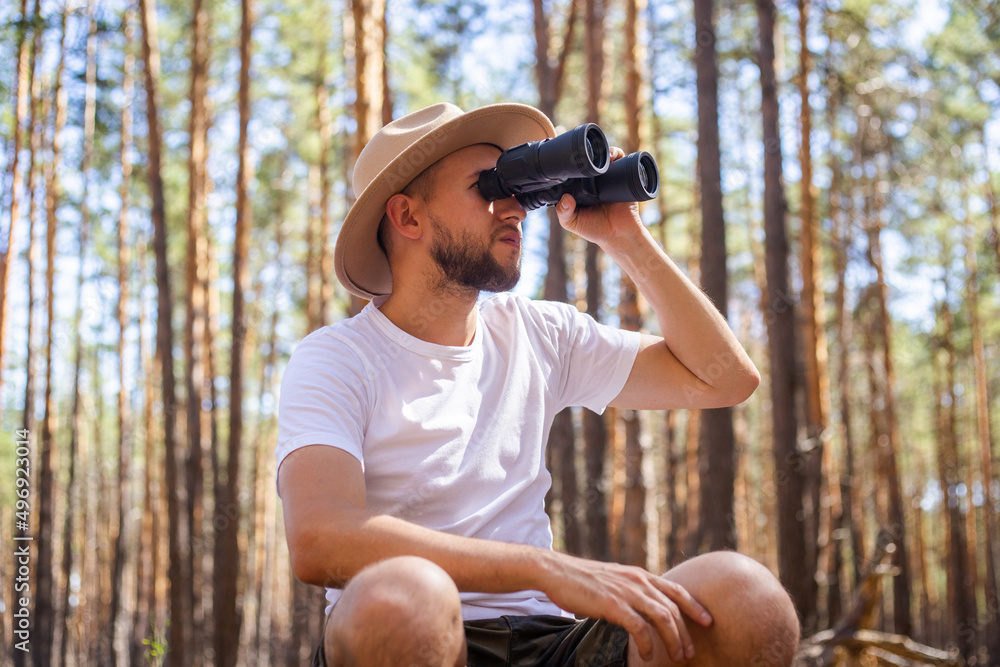 Man in a hat looks through binoculars during a camping trip. Hike in the mountains, forest