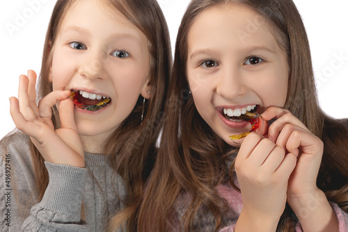 Two cute girls playfully pose with orthodontic appliances in their hands on a white background. The concept of oral hygiene in childhood.