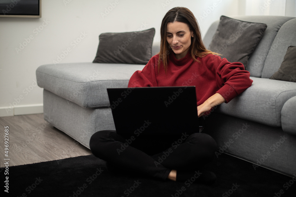 Woman using a laptop while relaxing in her apartment Woman using a laptop while relaxing in her apartment