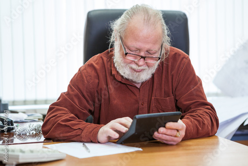 Caucasian man of retirement age counts on a calculator while sitting at table in office room