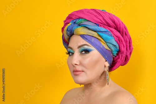 Portrait of a beautiful woman with blonde hair,brown eyes with professional makeup,jewelry,smiling with a colorful traditional shawl on her head.A woman with bare shoulders and a headscarf on her head