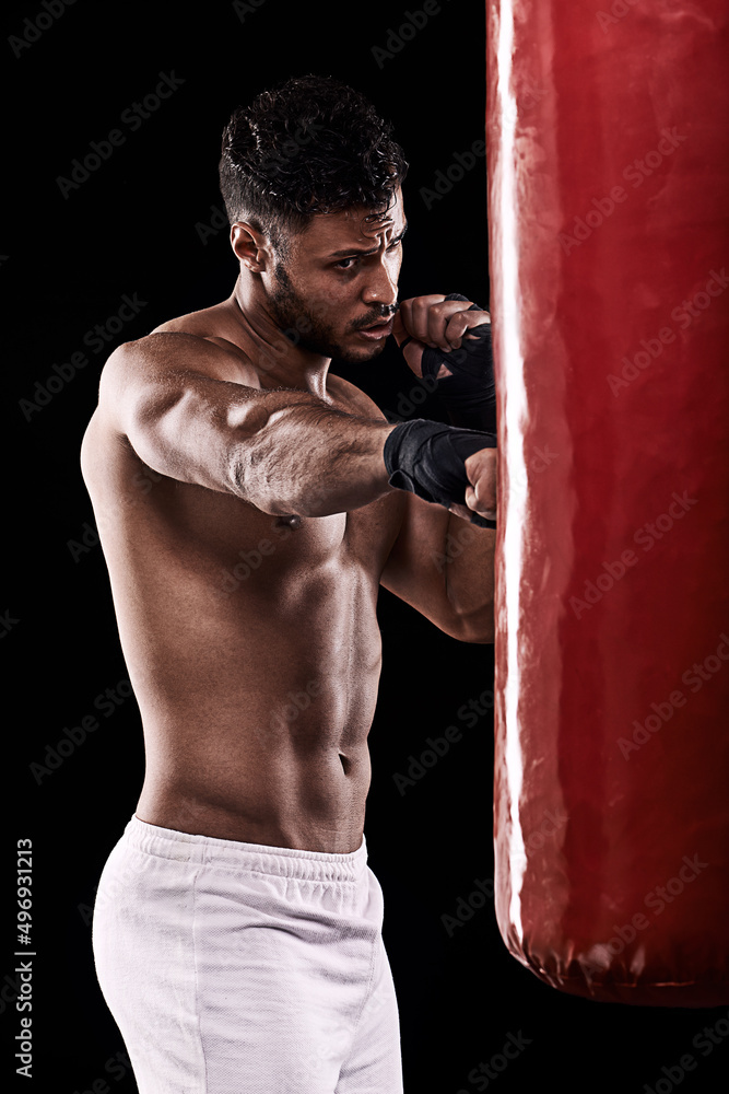 Its a long road to perfection. Studio shot of kick boxer working out with a punching bag against a black background.