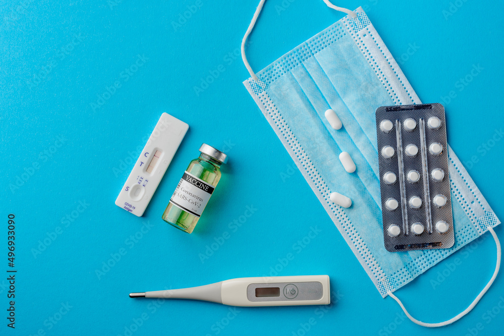 Fototapeta premium Flat lay on blue background with medical accessories - pills, covid-19 self-test kit and coronavirus vaccine ampoule