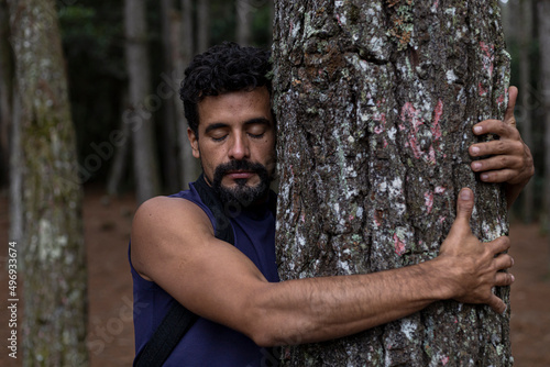 Valokuvatapetti Young Latin American man (37) with closed eyes hugs a tree in a pine forest