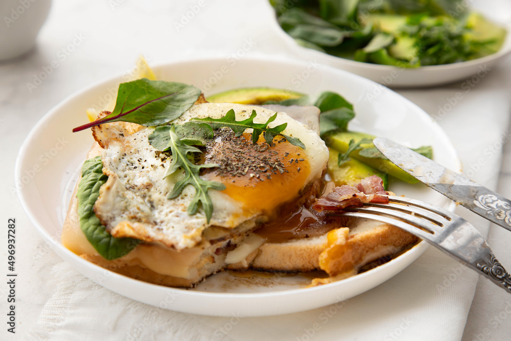 Croque madame sandwich with cheese, avocado and arugula close-up on a white plate. Croque madame sandwich with cheese, avocado and arugula close-up on a white plate.