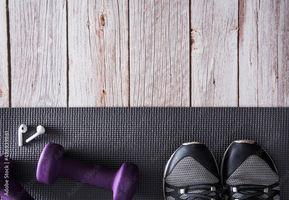 Fitness dumbbells, sneakers, and headphones on mat. Gym accessories. Copy space. Selective focus.