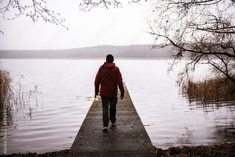 Mann läuft auf einem Steg abgewand auf einem See