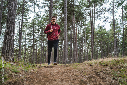 Front view full length of one man young caucasian male running trough the woods in nature outdoor jogging in autumn or spring day - sport fitness and recreation concept real people copy space