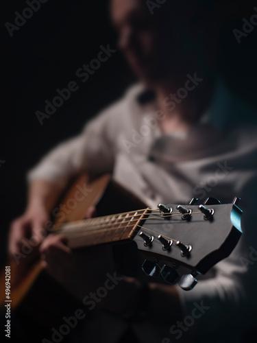 The guitarist is playing acoustic guitar shown in small depth of field where the focus is on the headstock. Dark and moody.