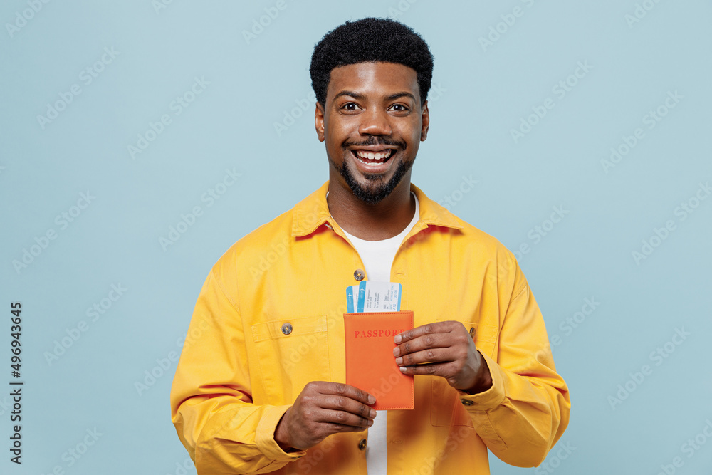 Traveler tourist man of African American ethnicity in yellow shirt hold passport ticket isolated on pastel plain blue background Passenger travel abroad on weekends getaway Air flight journey concept. Traveler tourist man of African American ethnicity in yellow shirt hold passport ticket isolated on pastel plain blue background Passenger travel abroad on weekends getaway Air flight journey concept.