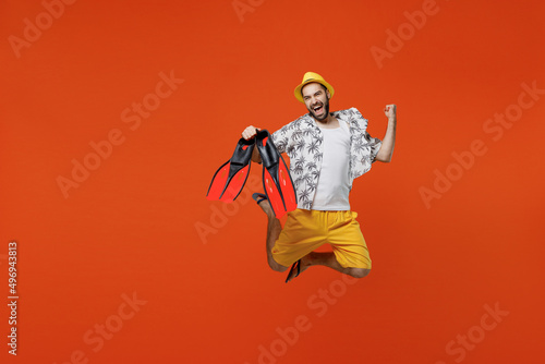 Full body exultant fun young tourist man in beach shirt goggles hold flippers jump high do winner gesture isolated on plain orange background studio portrait Summer vacation sea rest sun tan concept.