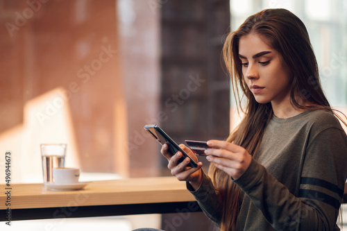 Woman using smartphone and a credit card for online shopping in a cafe