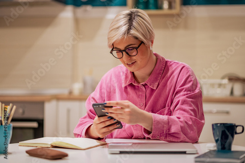 Short haired woman using smartphone in the kitchen at home