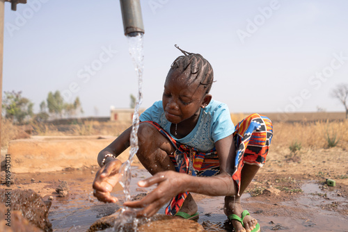 Thirsty African girl refreshes herself with cool drinking water from a village tap  water scarcity concept  pan-continental water shortage