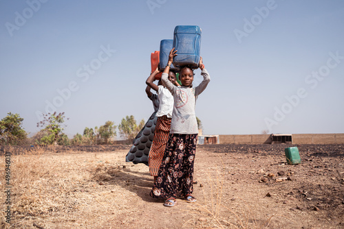 Small procession of girls in the rural African countryside engaged in the transport of drinking water from the distant borehole to their village photo