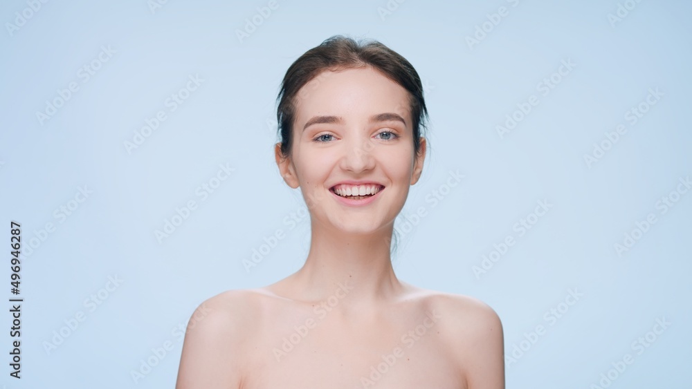 Young positive brunette woman looks at camera and smiles widely against blue seamless background | Skin care result concept Young positive brunette woman looks at camera and smiles widely against blue seamless background | Skin care result concept