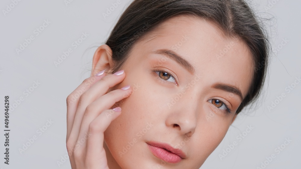 Extreme close-up beauty portrait of young dark-haired woman touches her face sliding fingers from a cheek down to her chin, looks at camera and smiles | Skincare product commercial concept Extreme close-up beauty portrait of young dark-haired woman touches her face sliding fingers from a cheek down to her chin, looks at camera and smiles | Skincare product commercial concept